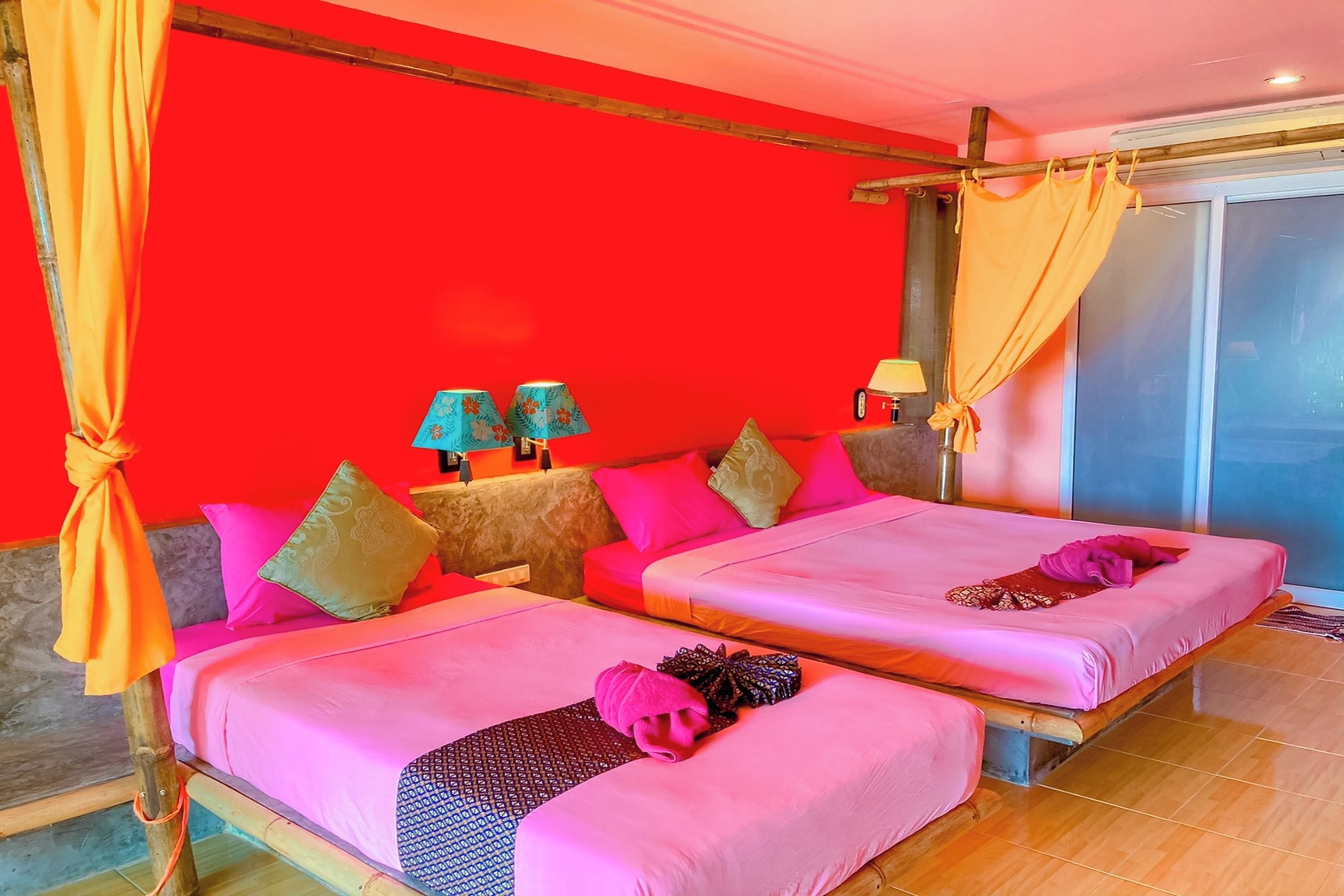 A room with two beds, each with pink bedding and multiple pillows. There are two lamps on side tables, and a curtain is tied to a wooden beam.
