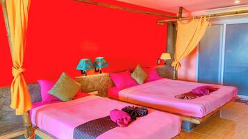 A room with two beds, each with pink bedding and multiple pillows. There are two lamps on side tables, and a curtain is tied to a wooden beam.
