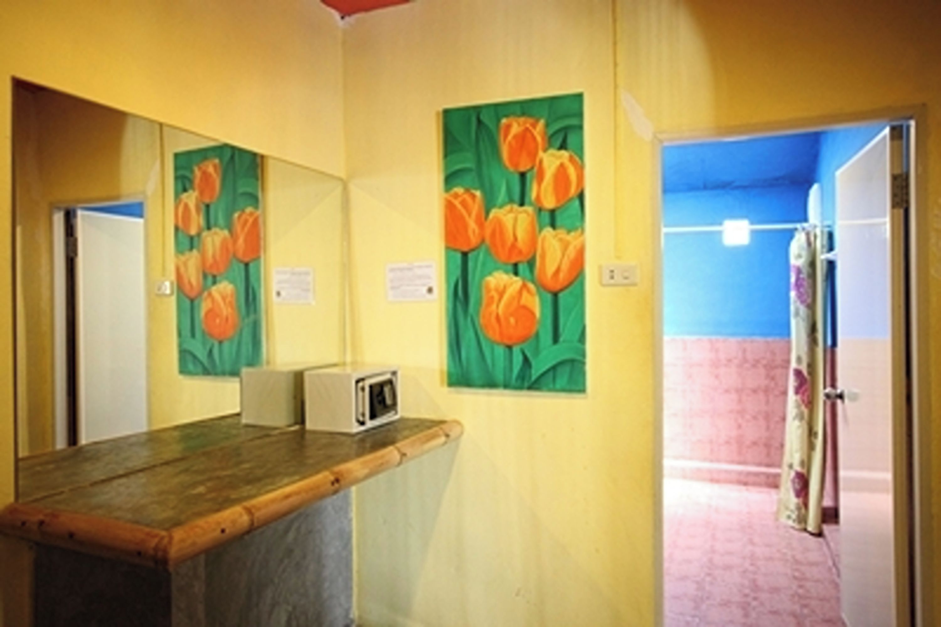 Een kamer met een houten bureau, een magnetron en een schilderij van oranje tulpen aan de muur.