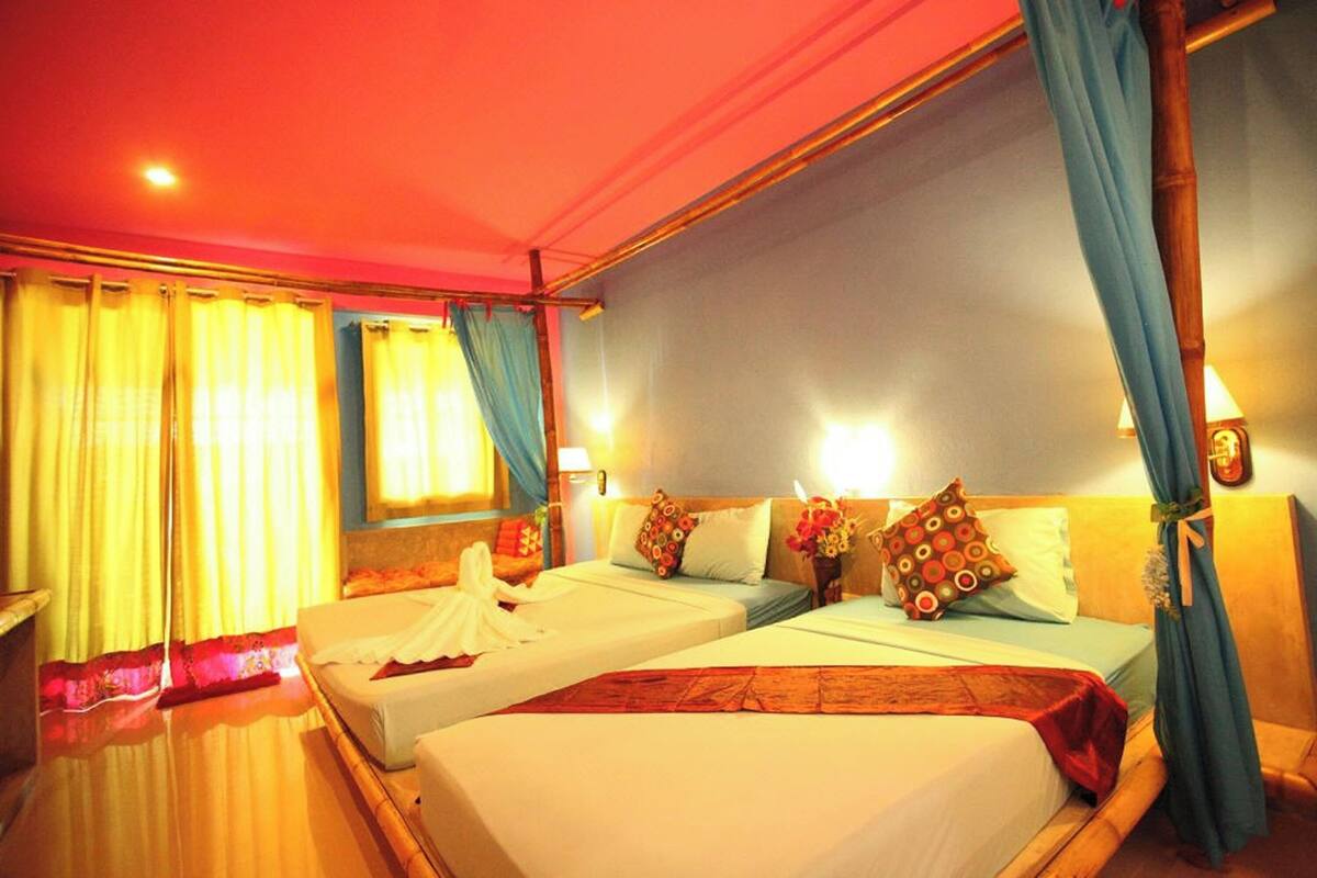 Habitación de hotel con dos camas, cabecero de madera, ventana con cortinas y una lámpara fijada a la pared.