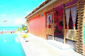 Un edificio frente a la playa con piscina, paredes coloridas y techo de paja.
