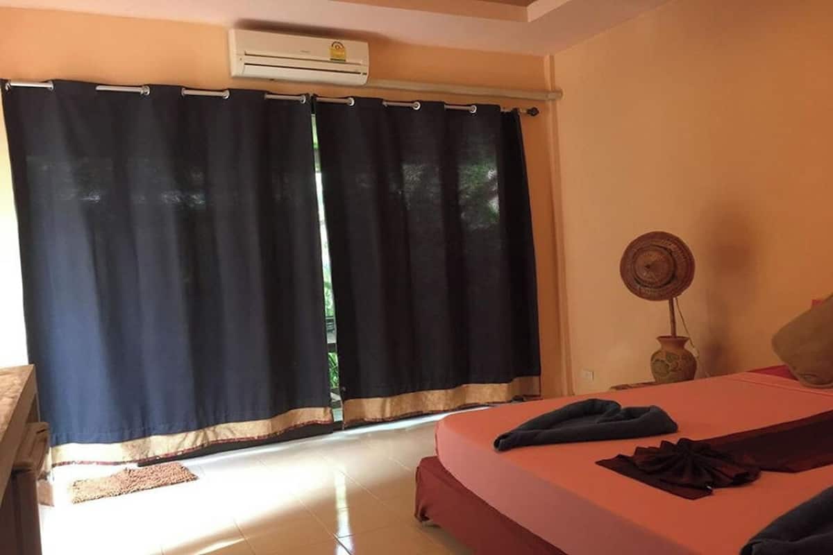 Una habitación con cama, ventana con cortinas, aire acondicionado y una pequeña mesa con un jarrón.
