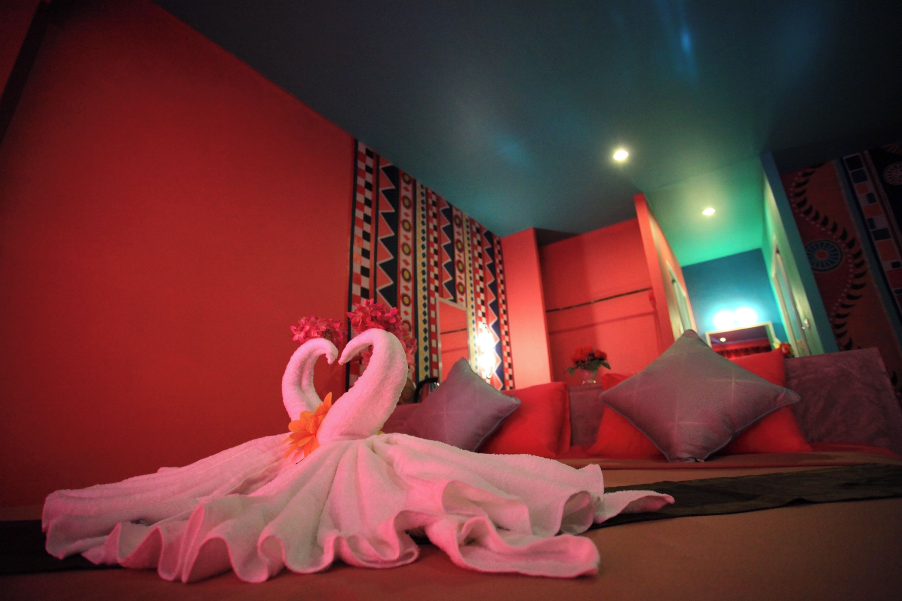 Habitación de hotel con cama, almohadas, pared con estampado geométrico y una toalla decorativa con forma de cisne.