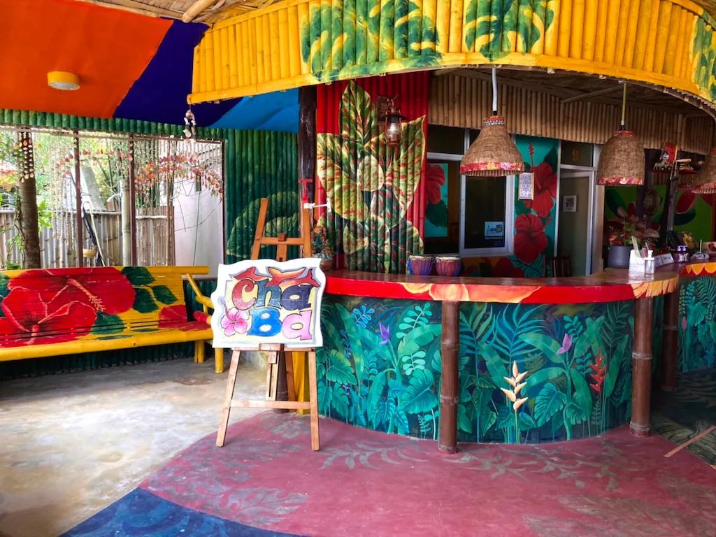 Uma área de bar vibrante com um mural tropical, um balcão de madeira e um letreiro que diz 'Coca Cola'.