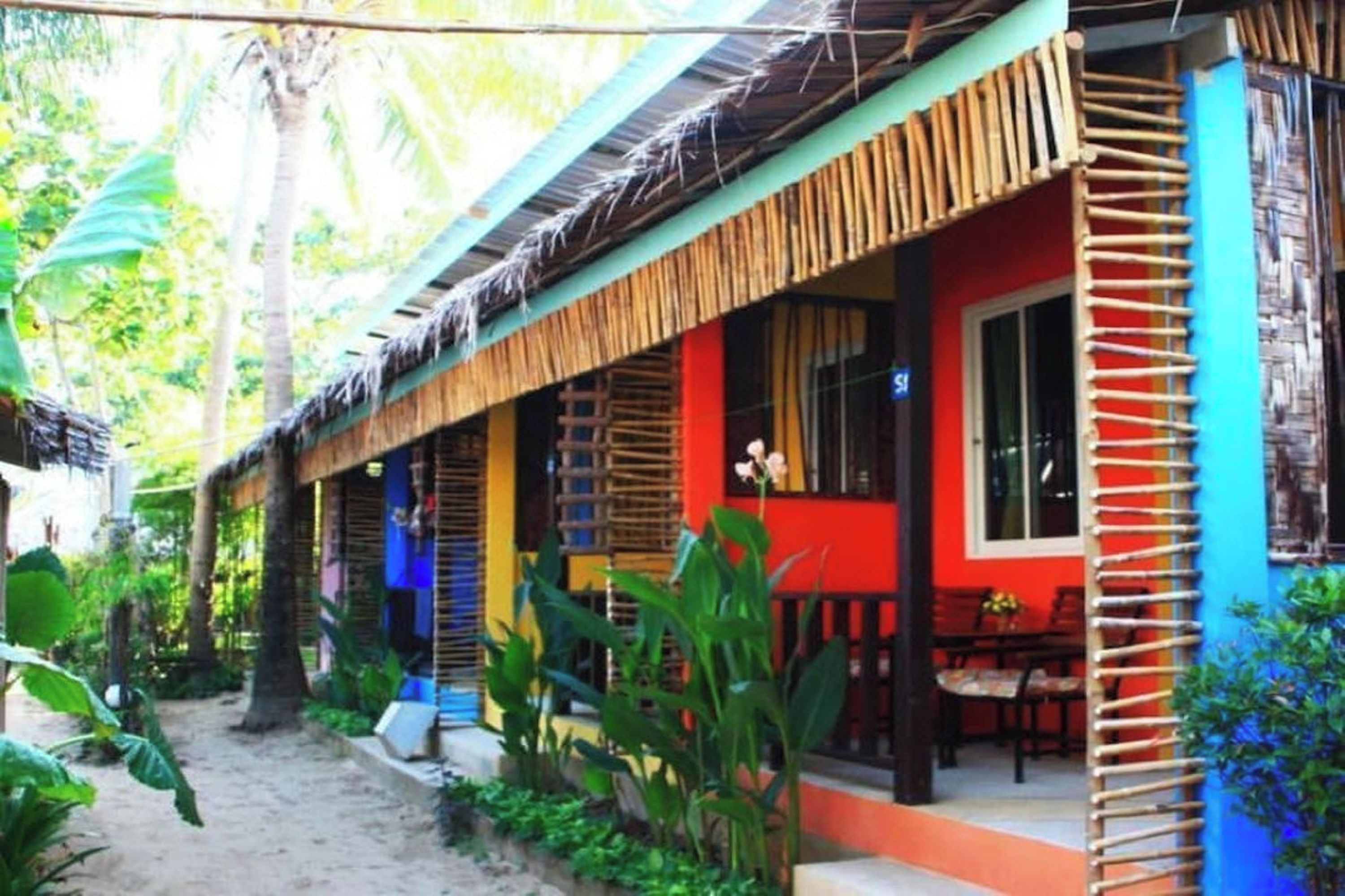 Un colorido bungalow con techo de paja, un pequeño porche y un jardín con plantas tropicales.