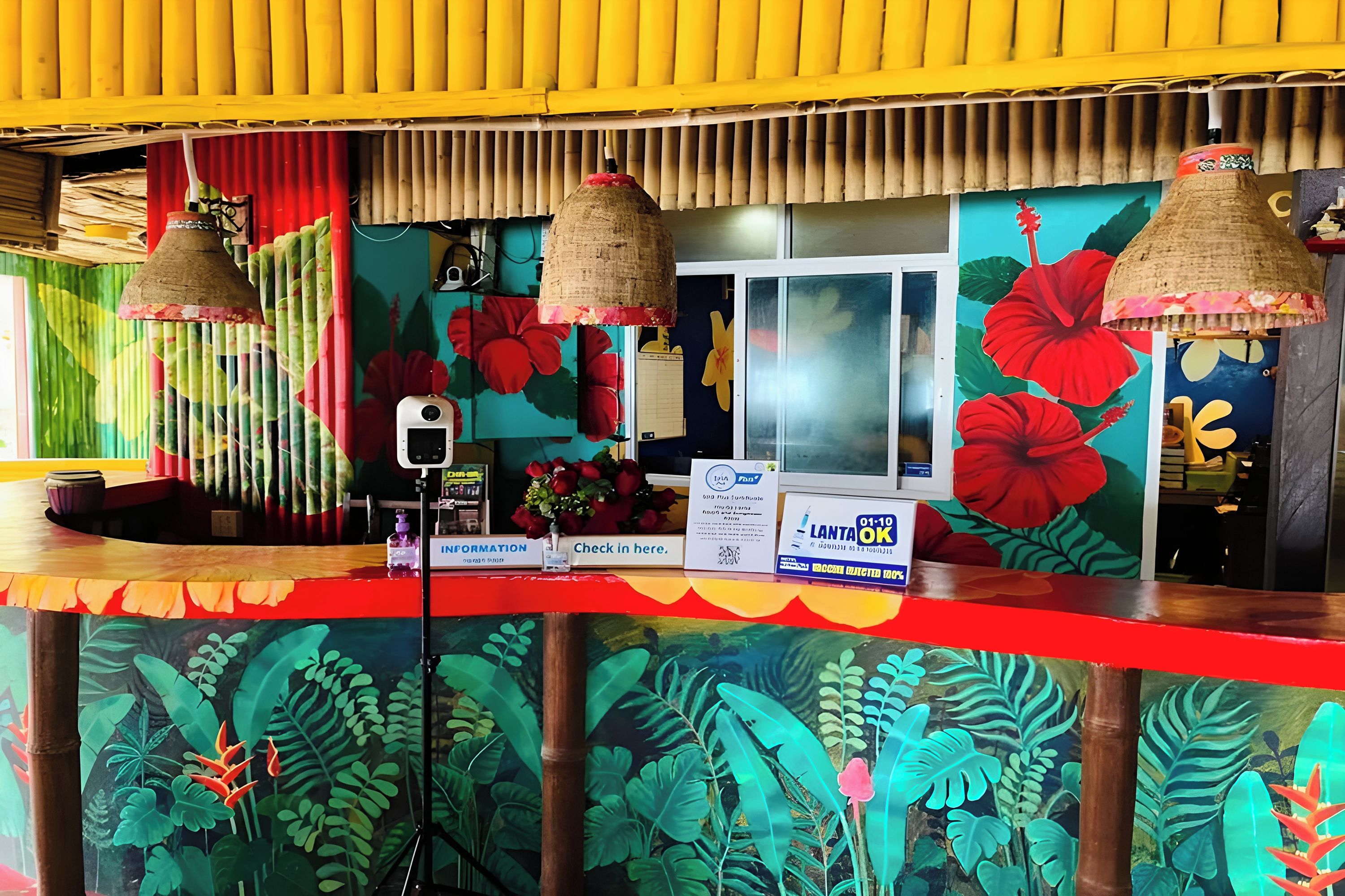 A reception area with a vibrant tropical mural, a check-in counter, and a sign indicating a 'LANTAN OF OK' service.