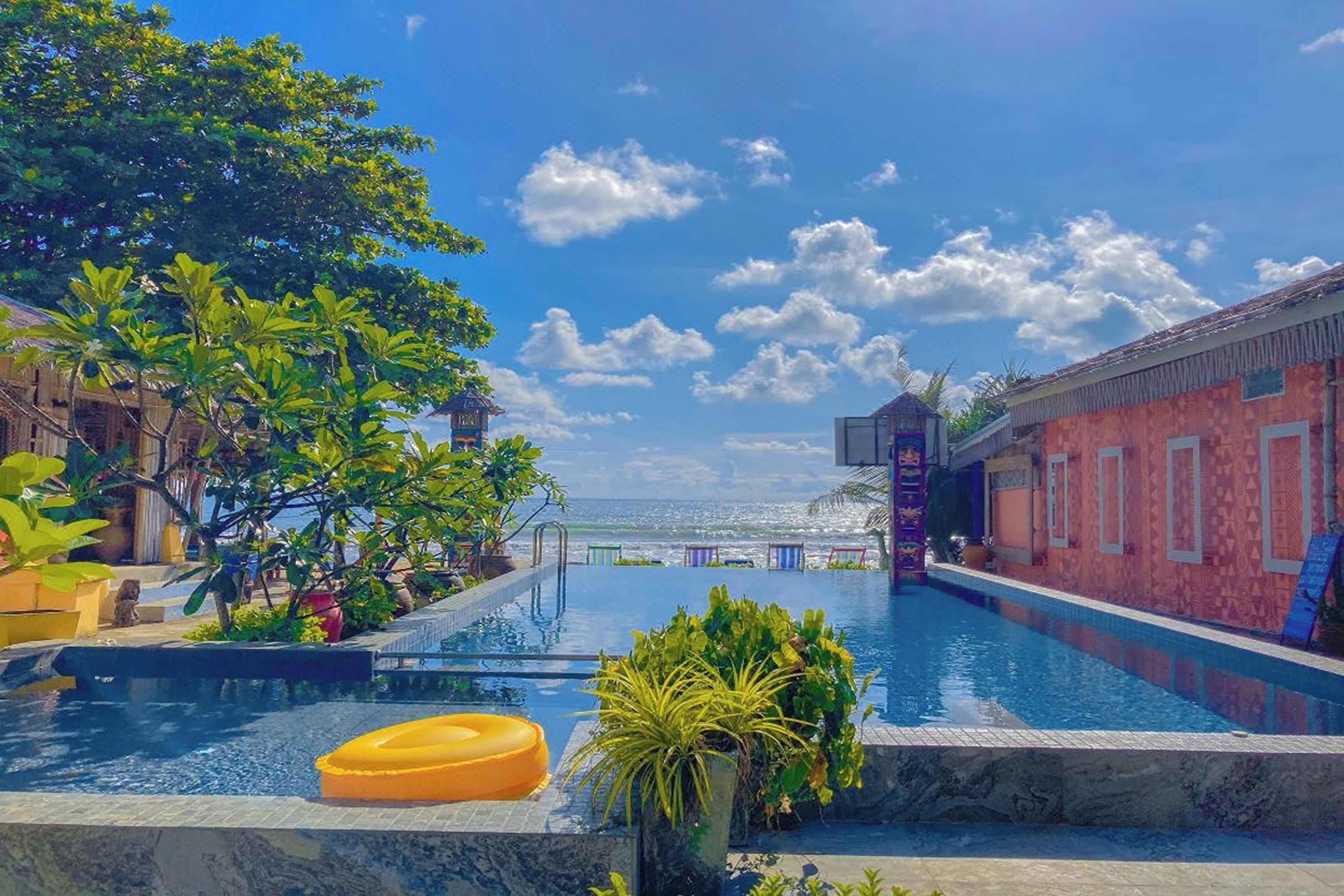 Una piscina con vistas despejadas al océano, rodeada de exuberante vegetación y un edificio con fachada decorativa.
