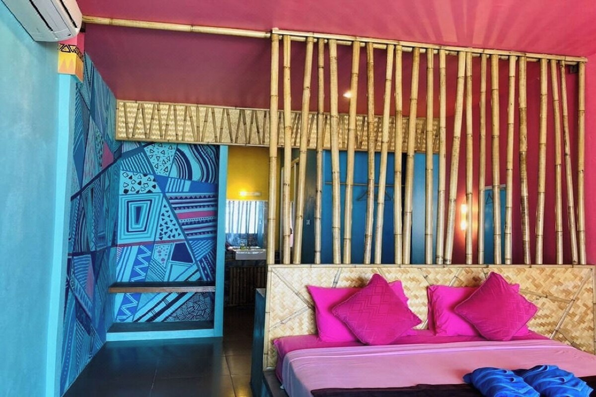 Una habitación con cama, separador de bambú y pared con diseños geométricos.