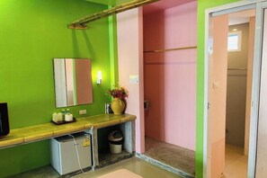 Une salle de bain avec un mur vert, un mur rose et un comptoir en bois avec un miroir. On y trouve une petite poubelle et un distributeur d’eau sur le comptoir.