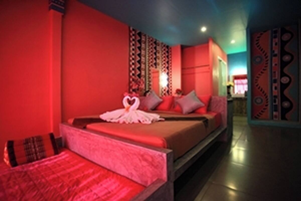 Una habitación con cama, almohadas, una mesita de noche y una pared con diseño decorativo.