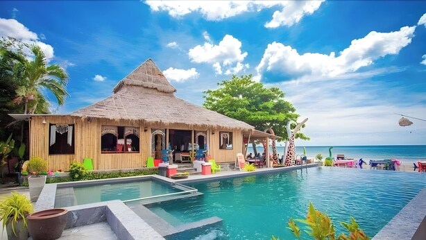 Un área junto a la piscina con una construcción de techo de paja, piscina y vista al océano.