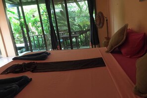 Una habitación con una cama, una ventana que da a zonas verdes y un ventilador en la pared.