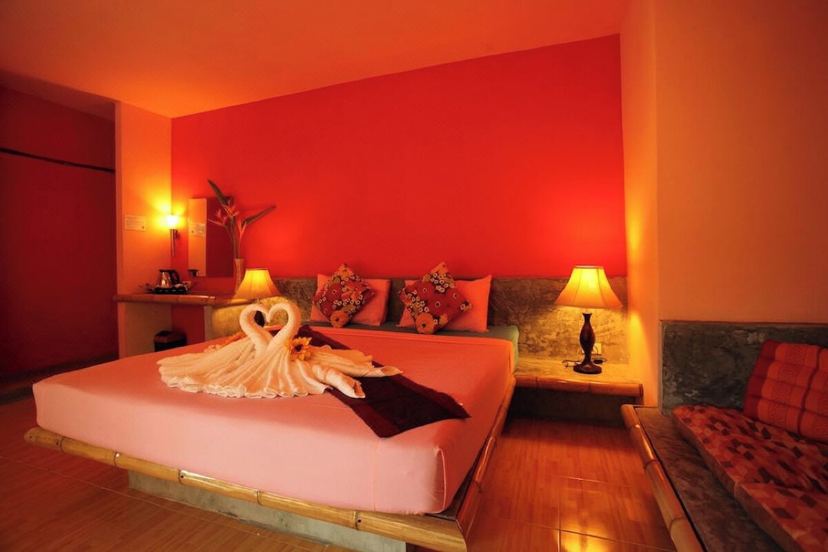 Habitación de hotel con una cama grande, dos mesitas de noche, un sofá y una pared de acento roja.