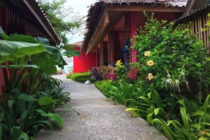 Un sentier mène à un bâtiment traditionnel doté d’un toit de chaume, entouré d’une végétation luxuriante et de plantes en fleurs.