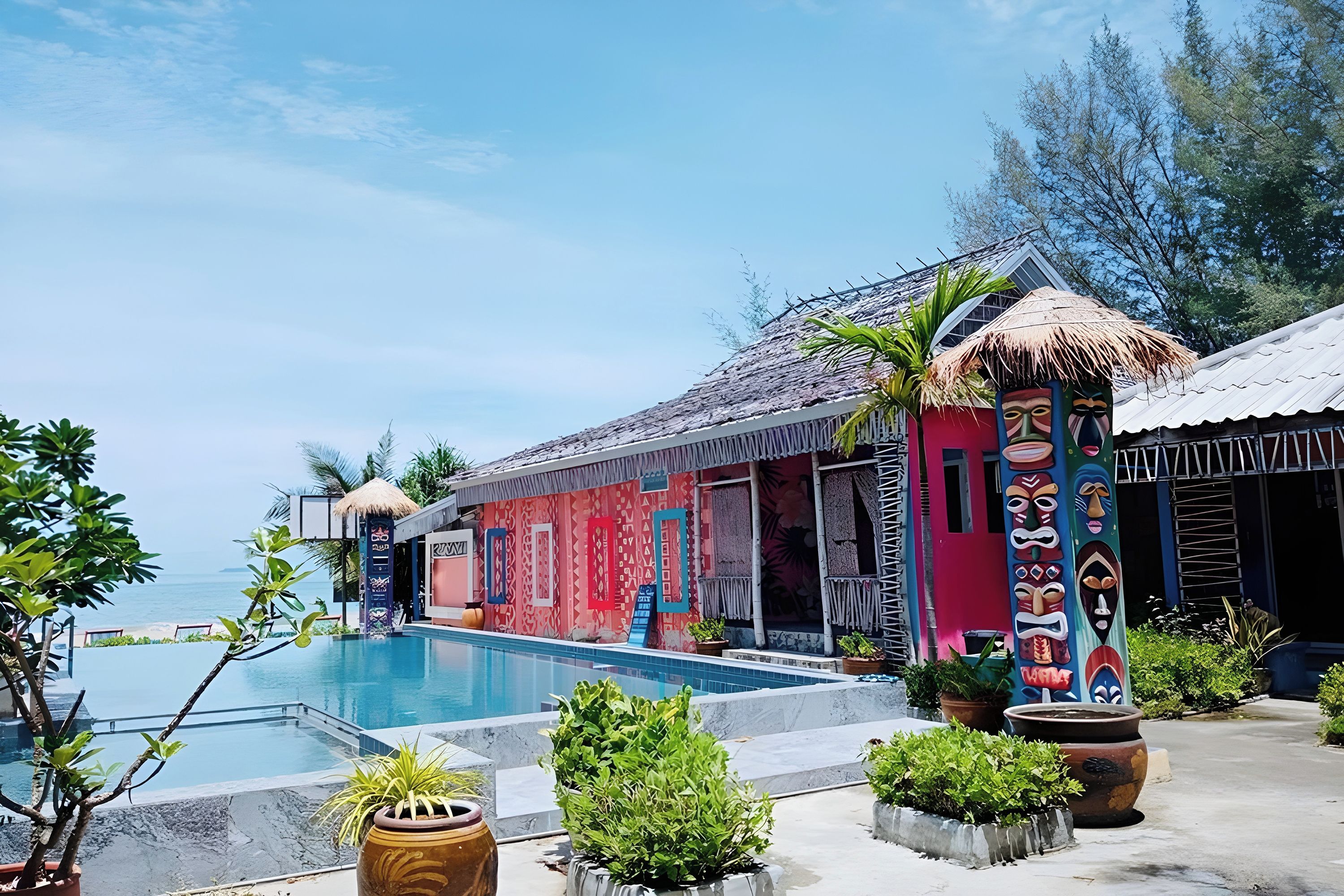 Zona de piscina con un edificio colorido, una estructura de techo de paja y vista al mar.