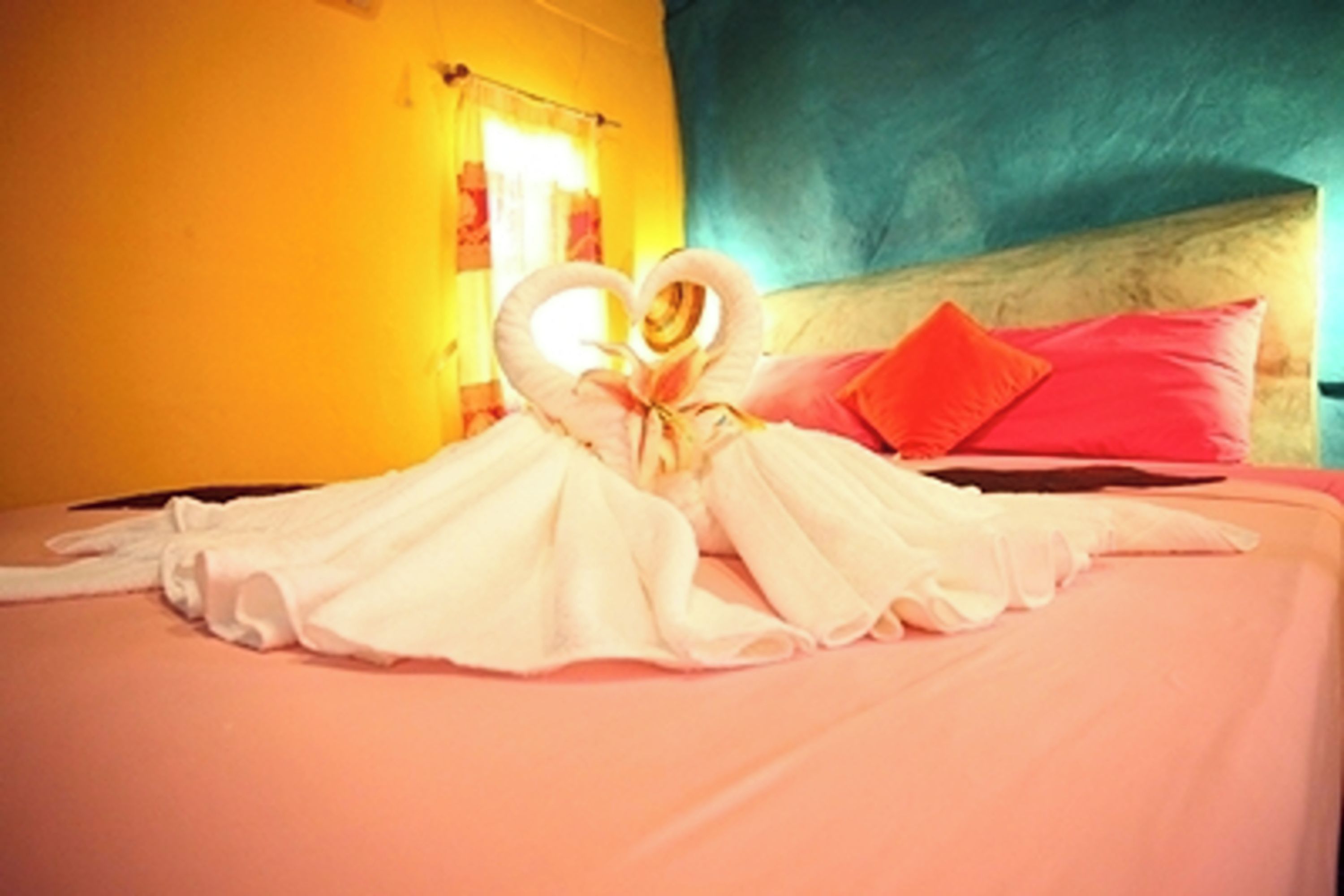 A bed with a heart-shaped towel arrangement and a red pillow.