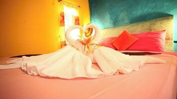 A bed with a heart-shaped towel arrangement and a red pillow.
