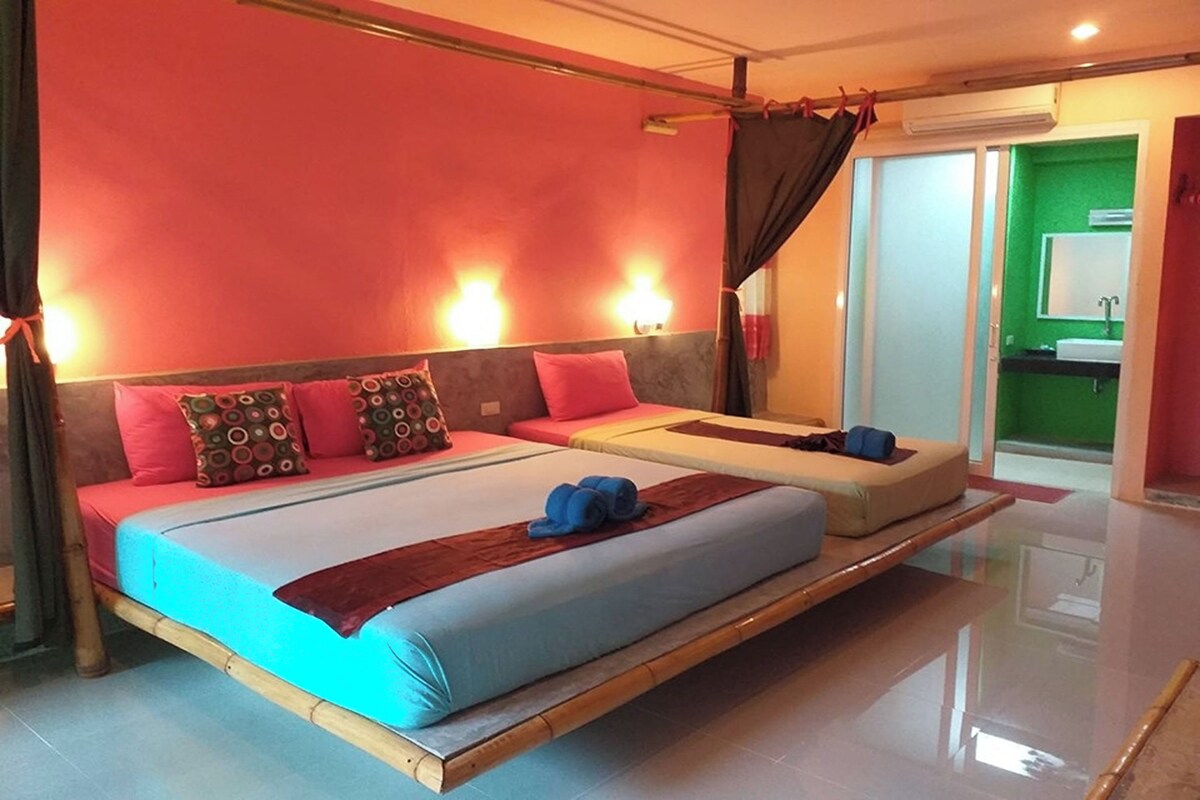 Una habitación de hotel moderna con una cama grande, una cama más pequeña, una tocador con espejo y una pared verde.