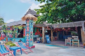 Un área de estar al aire libre, colorida, con estructuras de techo de paja y un bar tiki.