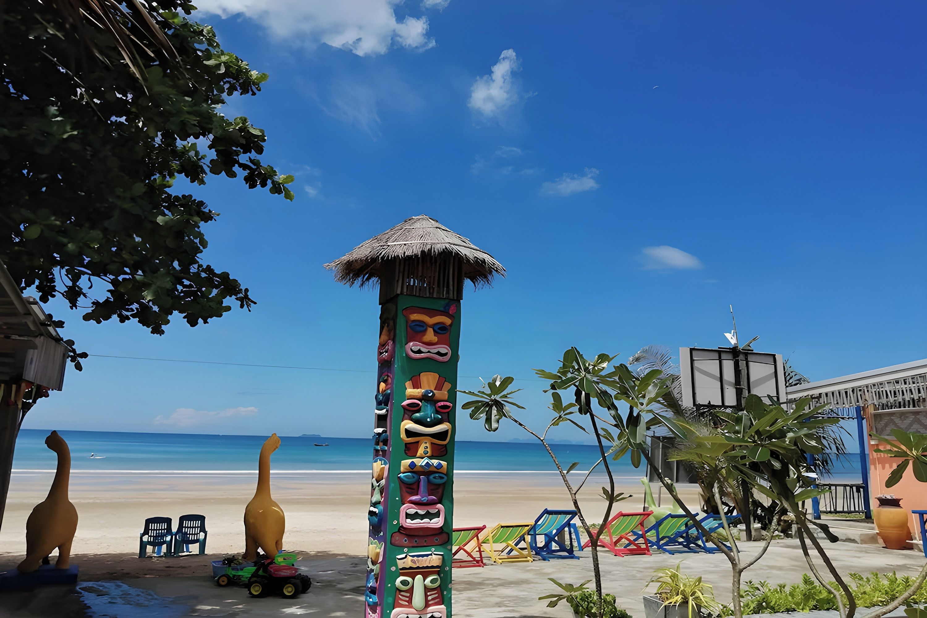 A beach scene with a decorated totem pole, beach chairs, and a small hut.