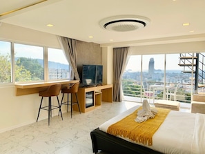 A modern hotel room with a large bed, a desk with two chairs, a TV, and a city view. - Oceanview Treasure Hotel And Residence (Patong)