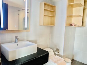 A bathroom with a white sink, a toilet, a shower, and wooden shelves. - Oceanview Treasure Hotel And Residence (Patong)