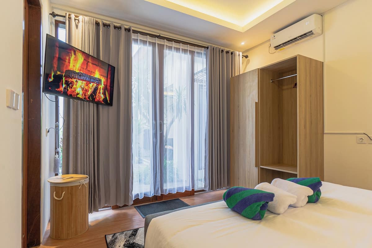 Habitación de hotel con cama, televisor en la pared, armario y ventana con cortinas.