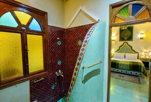 A room with a bed, a nightstand, a wall-mounted shelf, and a window with stained glass. - Casa De Marrakech Riad Guest House (Marrakech)