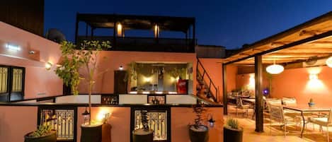 Un bar situé sur le toit, avec des places assises en plein air, des plantes en pot et un escalier menant à un niveau supérieur.