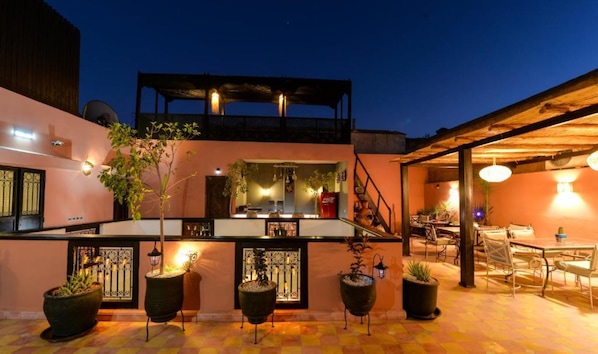 A rooftop bar with outdoor seating, potted plants, and a staircase leading to an upper level. - Casa De Marrakech Riad Guest House (Marrakech)