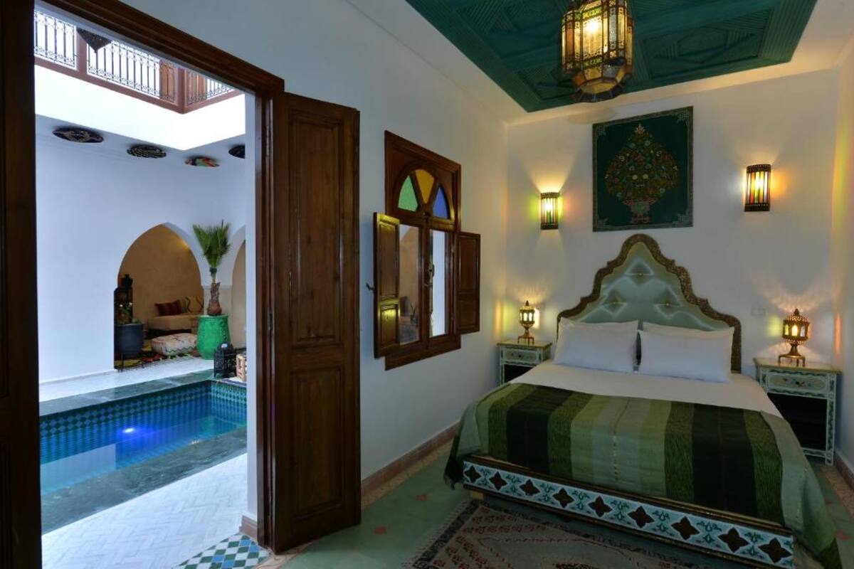 Una camera da letto con un letto grande, un comodino, una lampada a parete e vista su una piscina all'aperto.