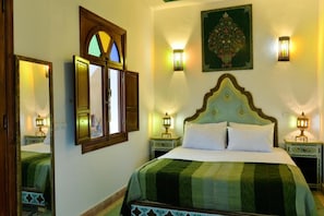 A bedroom with a bed, two nightstands, a mirror, a window with a stained glass design, and wall-mounted lamps. - Casa De Marrakech Riad Guest House (Marrakech)