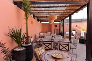 An outdoor patio with a wooden pergola, tables, chairs, and potted plants. - Casa De Marrakech Riad Guest House (Marrakech)