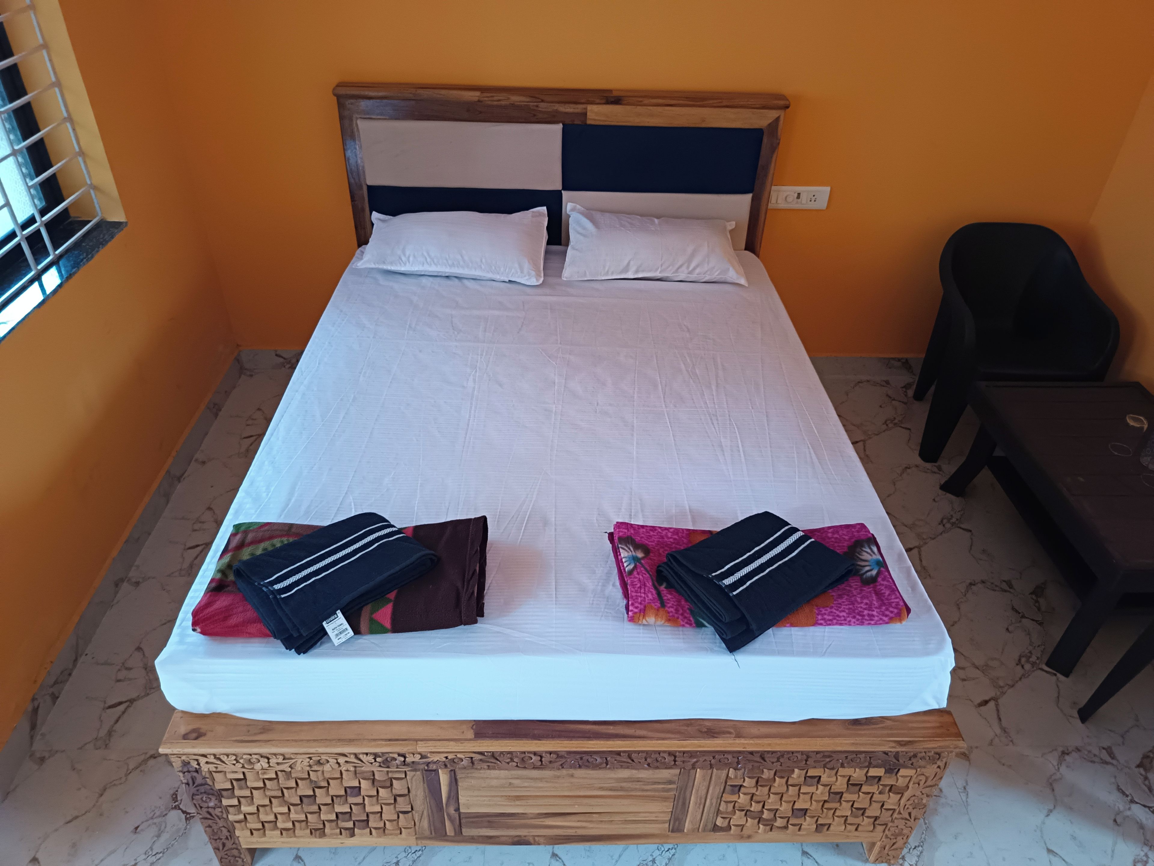 A bed with a wooden headboard, white bedding, and two pillows with folded clothes on them.