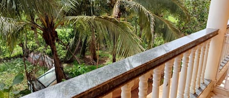 A balcony with a stone balustrade overlooking a garden with palm trees.
