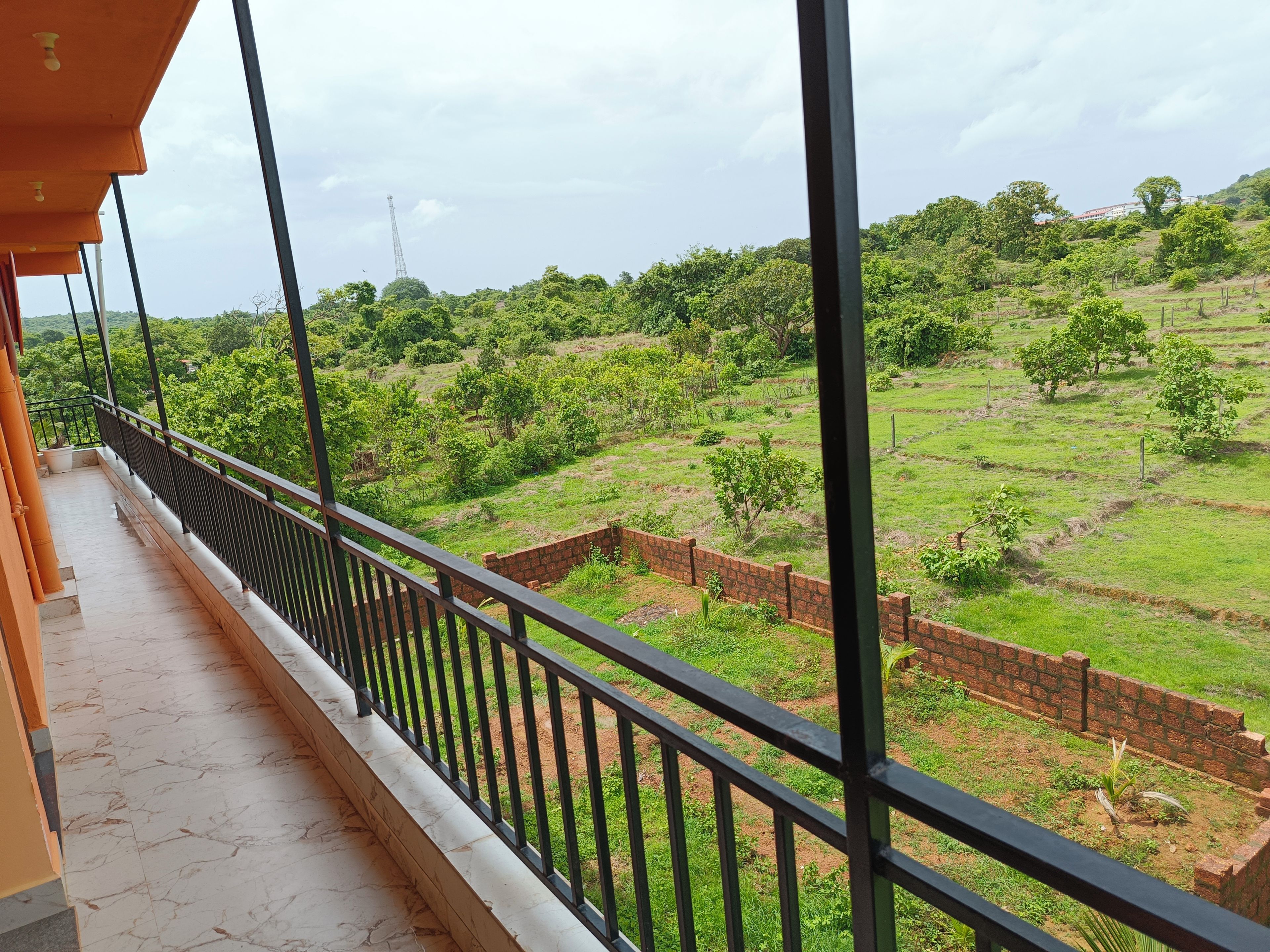 Un balcón con vista a un paisaje verde, un muro de ladrillo y una barandilla de metal.