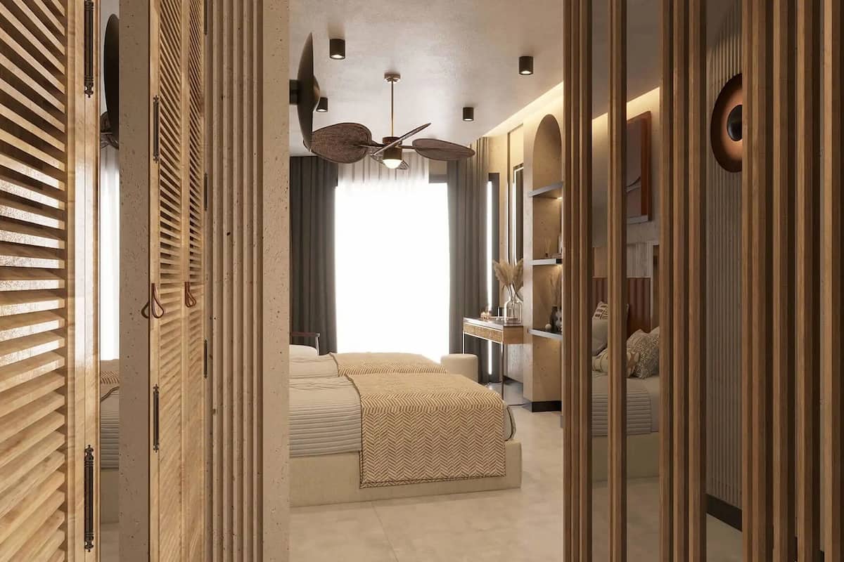 A walk-in closet with wooden slat doors, a bed with a patterned bedspread, a ceiling fan, and a mirror.