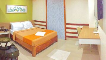 A hotel room with a bed, a desk, a chair, a small table, and a picture on the wall.