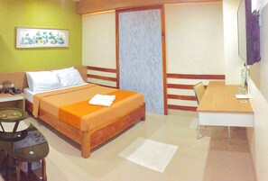 A hotel room with a bed, a desk, a chair, a small table, and a picture on the wall. - Reddoorz Plus @ Abc Landmark Hotel (Makilala)