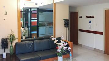 Un área de recepción con un sofá, una mesa de vidrio, un florero y un espejo, además de un cartel que indica las habitaciones 208 al 210.