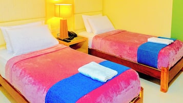 Two beds with pink and blue bedding, a bedside lamp, and a telephone on the nightstand.
