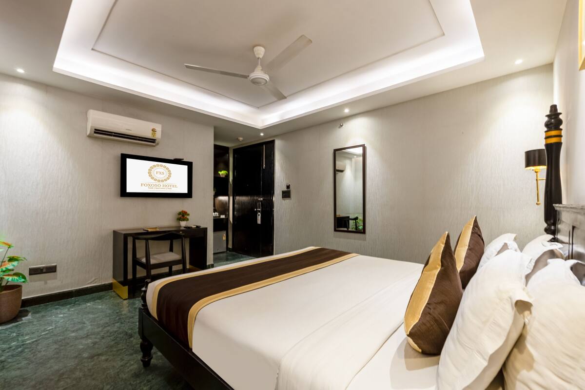 Ein Hotelzimmer mit Bett, Deckenventilator, Klimaanlage, Schreibtisch, Spiegel und Fernseher.