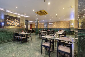 A restaurant with marble flooring, multiple tables and chairs, and a large floral painting on the wall. - Foxoso Hotel Delhi Airport (New Delhi)