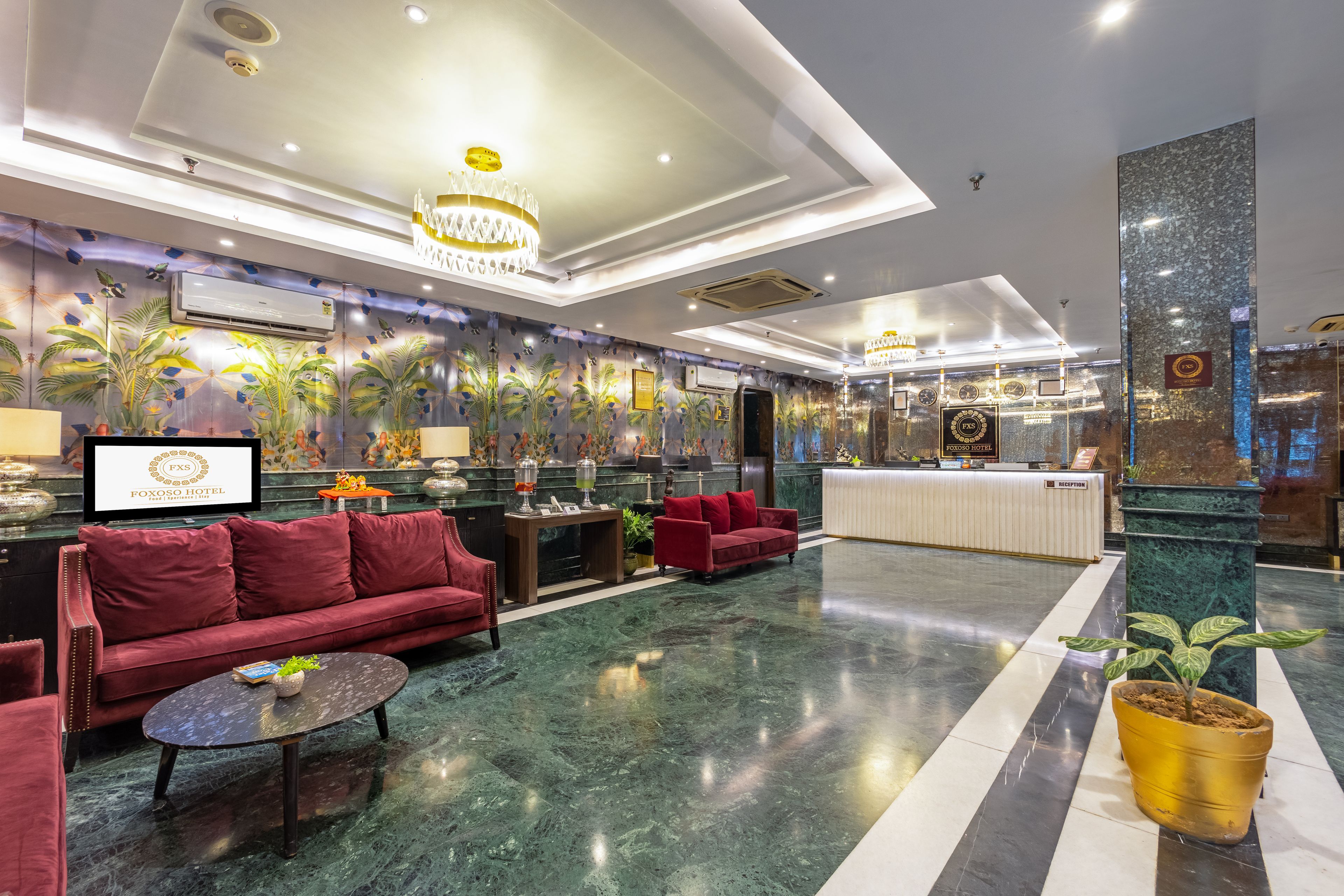 A hotel lobby with a reception desk, red sofas, a coffee table, and a large chandelier.