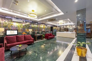 A hotel lobby with a reception desk, red sofas, a coffee table, and a large chandelier. - Foxoso Hotel Delhi Airport (New Delhi)