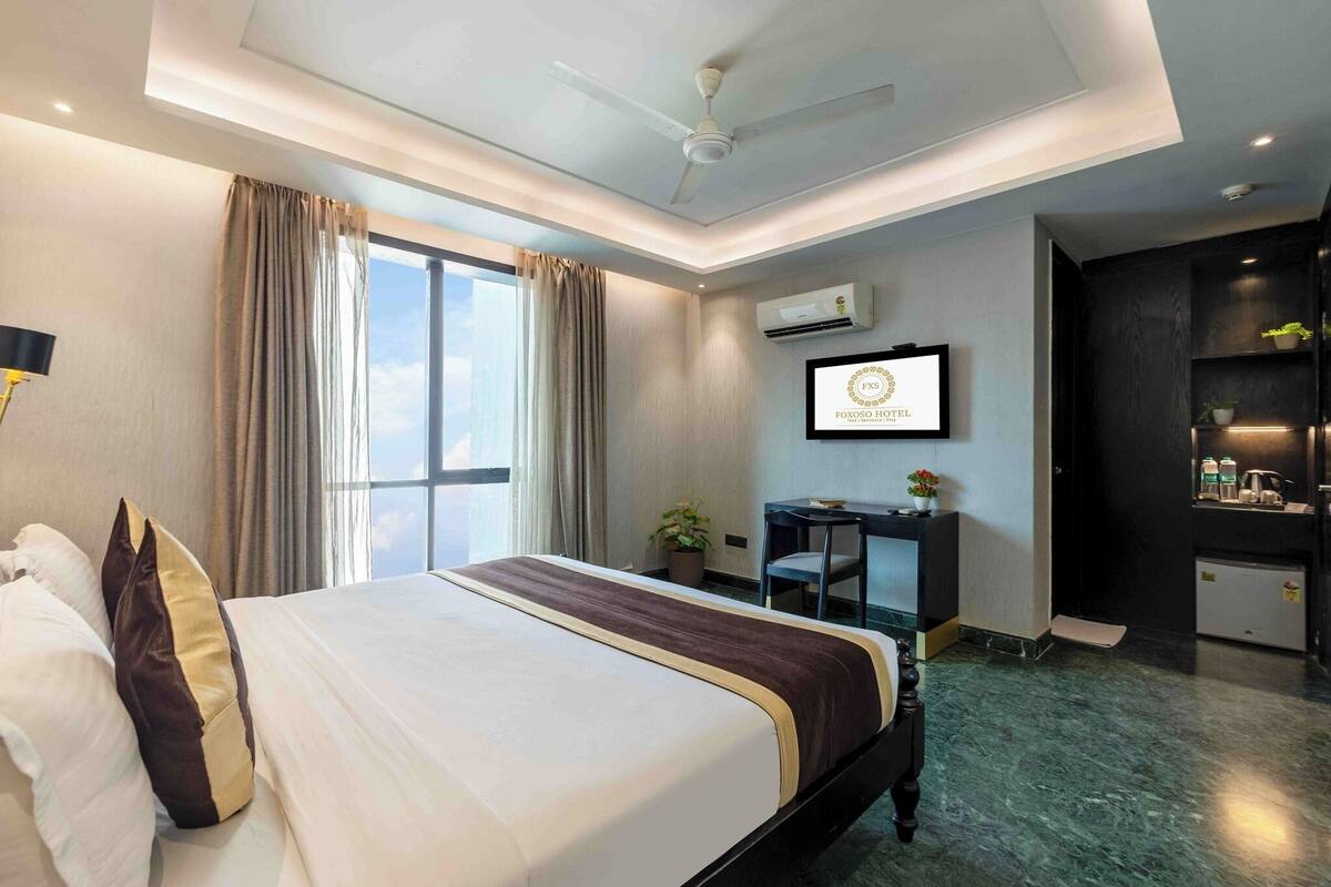 Ein Hotelzimmer mit Bett, Schreibtisch, Stuhl, Deckenventilator, Klimaanlage und Blick auf den Himmel.