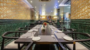 A restaurant with a long table set for dining, marble walls, and a chandelier. - Foxoso Hotel Delhi Airport (New Delhi)