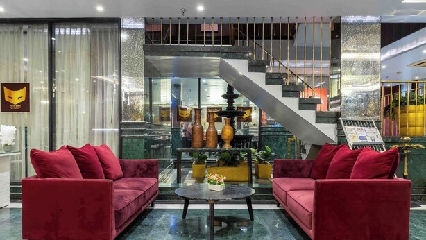 A lobby with two red sofas, a marble coffee table, and a staircase. - Foxoso Hotel Delhi Airport (New Delhi)