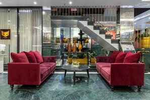 Um hall com dois sofás vermelhos, uma mesa de centro de mármore e uma escadaria.