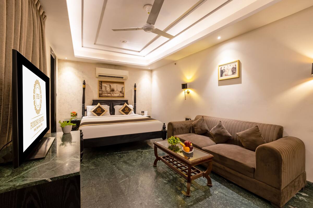 Ein Hotelzimmer mit Bett, Sofa, Couchtisch, Fernseher und Deckenventilator.